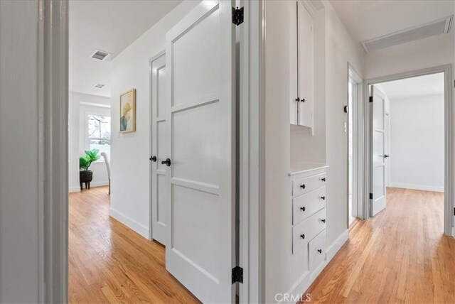 corridor featuring baseboards, light wood-style flooring, and visible vents