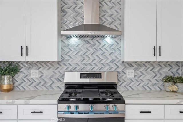kitchen featuring white cabinetry, gas range, light stone countertops, backsplash, and wall chimney range hood