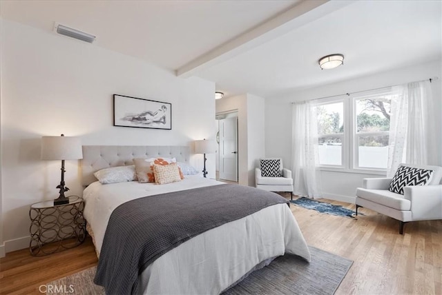 bedroom with baseboards, beamed ceiling, visible vents, and wood finished floors