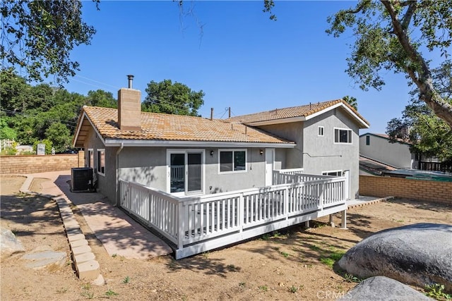back of house with a deck, stucco siding, a tiled roof, a chimney, and central AC unit