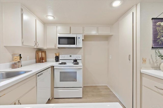 kitchen featuring white cabinets, light countertops, light wood-style floors, and white appliances