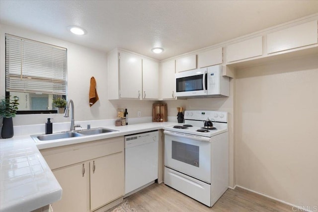 kitchen with white cabinetry, light wood-style floors, a sink, and white appliances