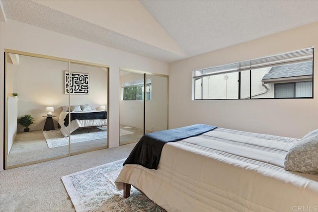 carpeted bedroom featuring lofted ceiling and two closets
