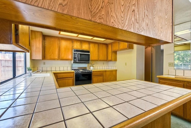 kitchen featuring a sink, brown cabinetry, tile countertops, black microwave, and range with gas cooktop