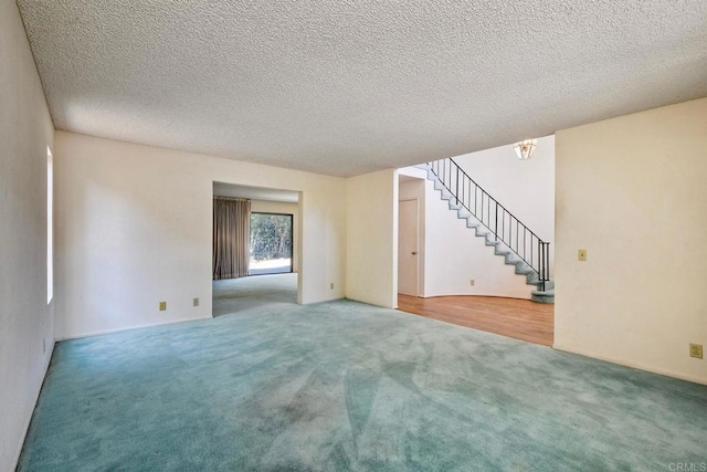 unfurnished living room featuring carpet, a textured ceiling, and stairway