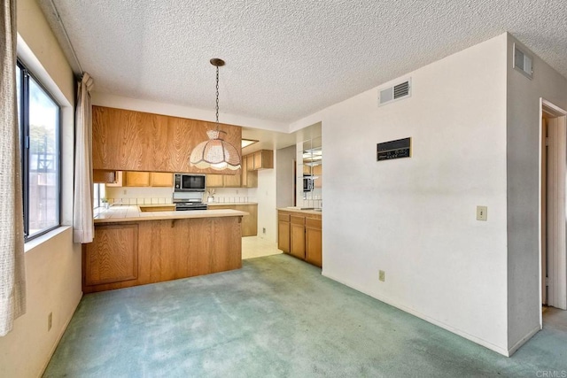 kitchen featuring built in microwave, visible vents, a peninsula, brown cabinets, and light colored carpet