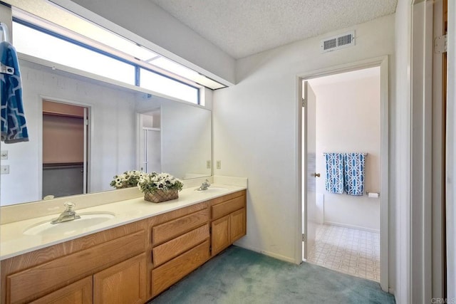 bathroom with double vanity, a textured ceiling, visible vents, and a sink