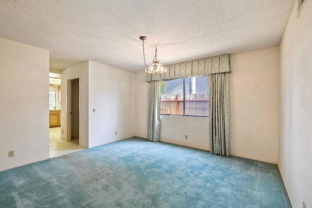 empty room featuring a textured ceiling, carpet, a notable chandelier, and plenty of natural light