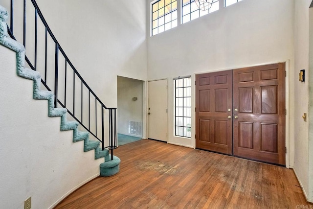 entryway featuring a wealth of natural light, stairway, a towering ceiling, and wood finished floors