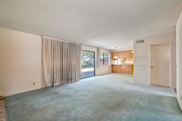unfurnished living room featuring a textured ceiling, visible vents, and light colored carpet