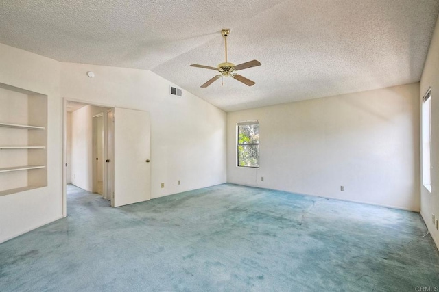 carpeted spare room with a textured ceiling, visible vents, ceiling fan, built in shelves, and lofted ceiling
