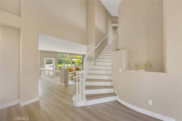 stairs featuring a towering ceiling, baseboards, and wood finished floors