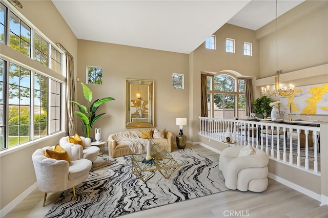 living room with a towering ceiling, a notable chandelier, baseboards, and wood finished floors