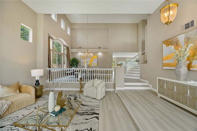 living area featuring wood finished floors, visible vents, stairway, an inviting chandelier, and a high ceiling