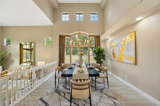 dining area with a chandelier, wood finished floors, baseboards, and a high ceiling