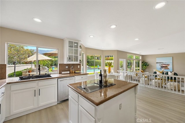kitchen with stainless steel dishwasher, a sink, a kitchen island, black electric stovetop, and light wood-type flooring