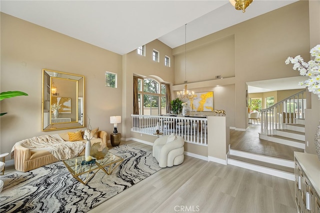 living room with an inviting chandelier, a wealth of natural light, light wood-style flooring, and a towering ceiling