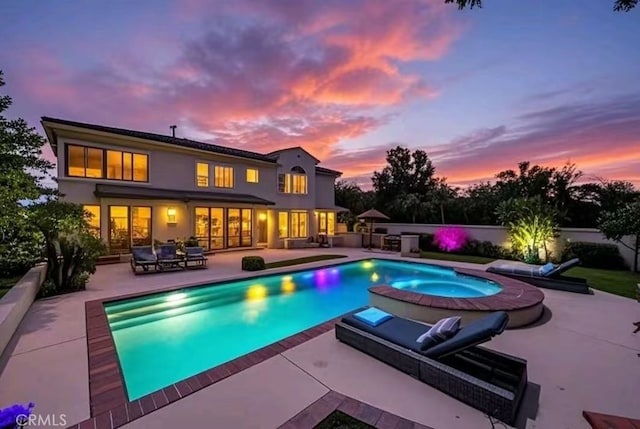 pool at dusk featuring outdoor lounge area, a patio, an in ground hot tub, and an outdoor pool