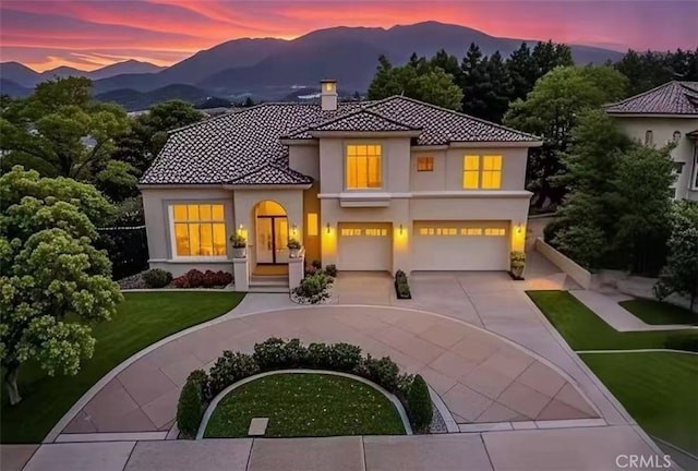mediterranean / spanish home with a chimney, a mountain view, an attached garage, stucco siding, and curved driveway