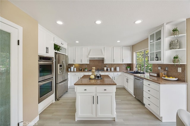 kitchen featuring custom exhaust hood, a sink, open shelves, a kitchen island, and appliances with stainless steel finishes