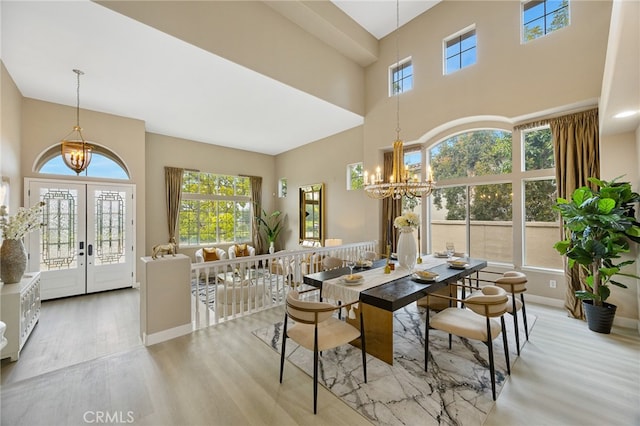 dining space featuring french doors, wood finished floors, a high ceiling, a notable chandelier, and baseboards