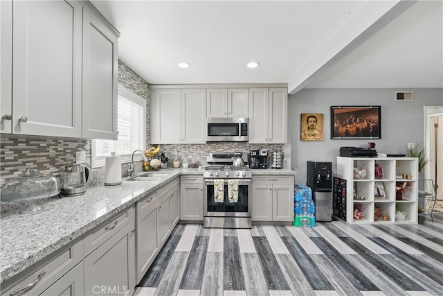 kitchen featuring a sink, visible vents, light stone countertops, backsplash, and appliances with stainless steel finishes
