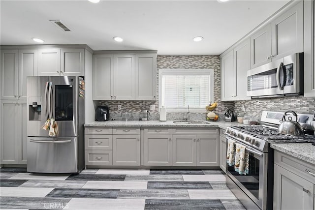 kitchen with a sink, stainless steel appliances, tasteful backsplash, gray cabinets, and visible vents