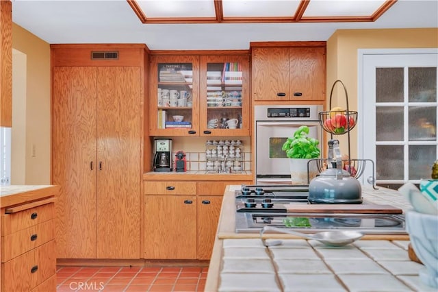 kitchen featuring oven, tile countertops, visible vents, glass insert cabinets, and light tile patterned floors