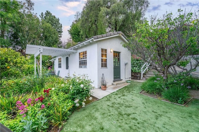 back of house with a lawn, stucco siding, and a pergola