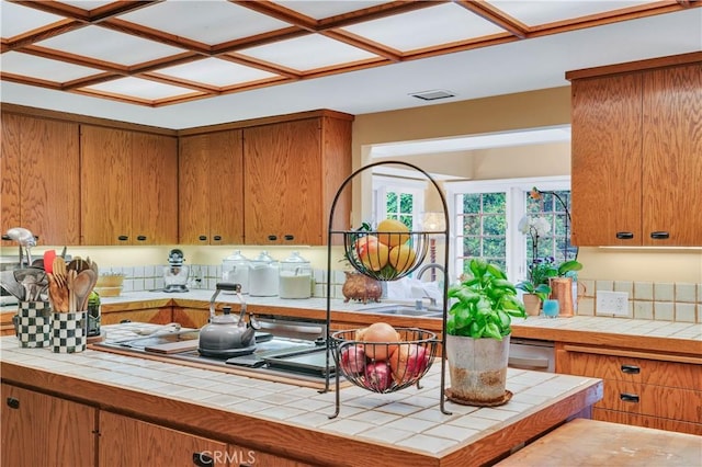 kitchen featuring tile countertops, brown cabinetry, stovetop, and a sink