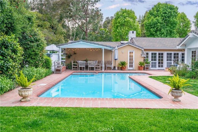 pool with a lawn, a patio area, outdoor dining area, and french doors
