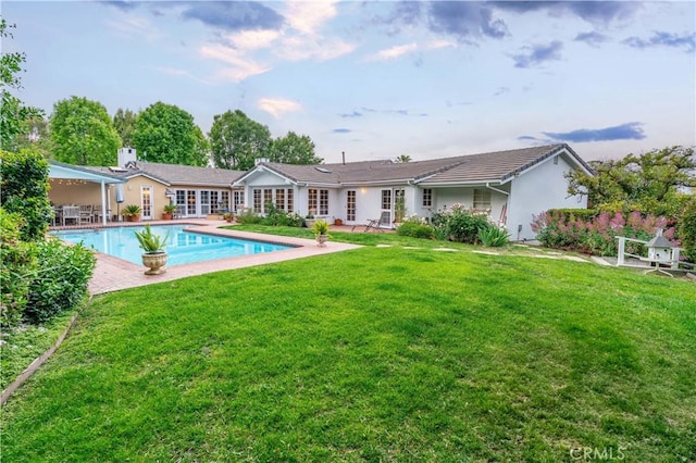 rear view of house featuring a lawn, a patio, stucco siding, and an outdoor pool