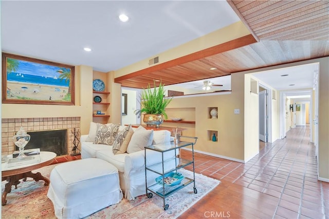 tiled living area with visible vents, built in shelves, a ceiling fan, baseboards, and a tiled fireplace