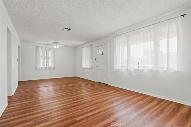 empty room featuring wood finished floors, a textured ceiling, visible vents, ceiling fan, and baseboards