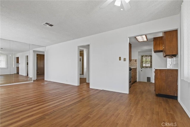 unfurnished living room with a ceiling fan, a textured ceiling, baseboards, visible vents, and wood finished floors