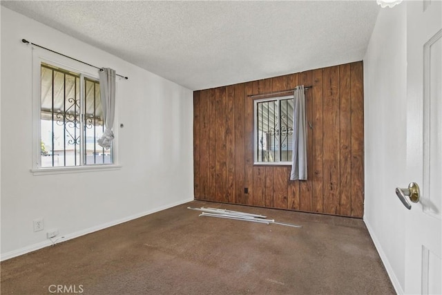 unfurnished room with a textured ceiling, wooden walls, and baseboards