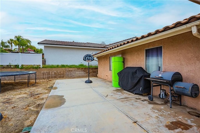 view of patio with a trampoline, grilling area, and fence