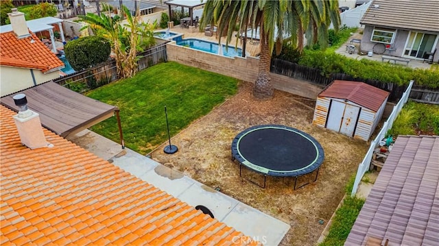 view of community featuring an outdoor structure, a trampoline, a storage unit, a fenced backyard, and a lawn