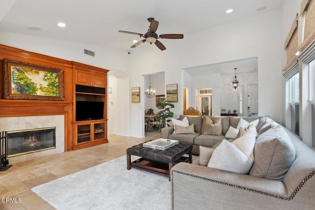 living area with ceiling fan with notable chandelier, a high ceiling, a tiled fireplace, visible vents, and recessed lighting
