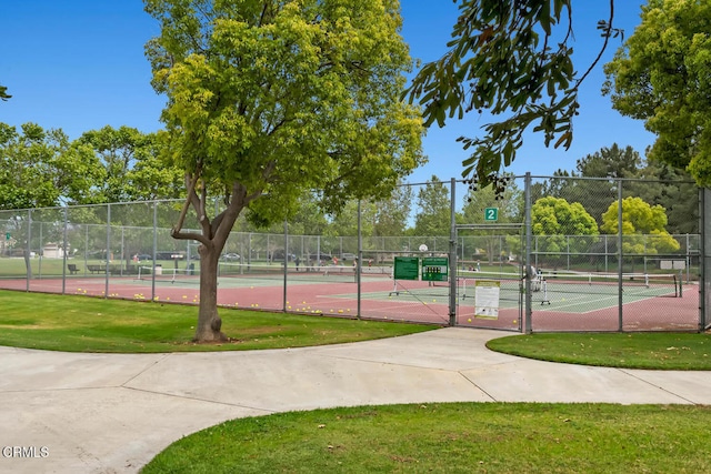 view of tennis court with a yard and fence