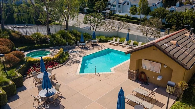 community pool with a patio area, fence, and a hot tub