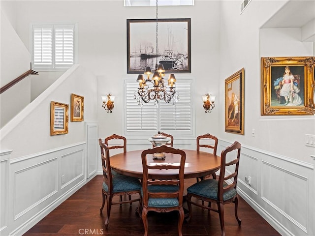 dining space featuring a chandelier, dark wood-type flooring, a decorative wall, a wainscoted wall, and a towering ceiling