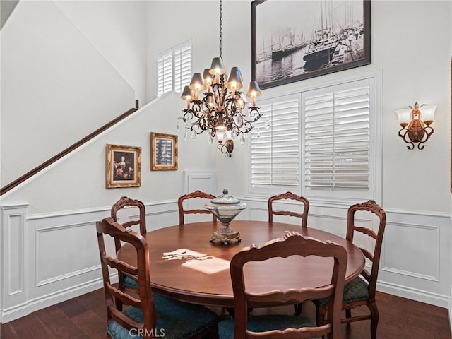 dining space with a decorative wall, a chandelier, wood finished floors, a wainscoted wall, and a towering ceiling