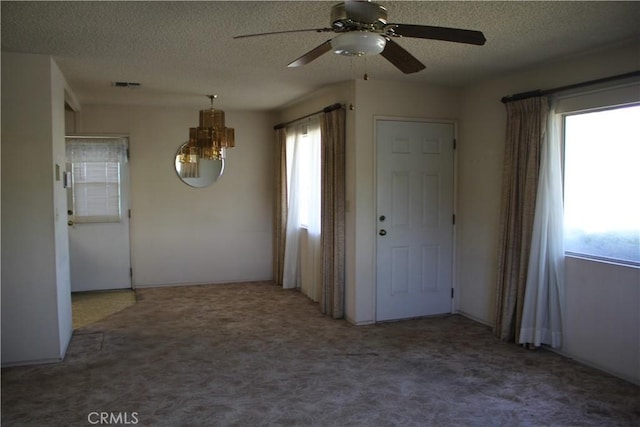 empty room with a textured ceiling, carpet flooring, ceiling fan with notable chandelier, and visible vents