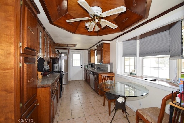 kitchen featuring ceiling fan, crown molding, light tile patterned floors, stainless steel dishwasher, and dark countertops