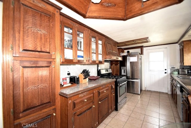 kitchen with glass insert cabinets, light tile patterned flooring, backsplash, dark countertops, and stainless steel appliances