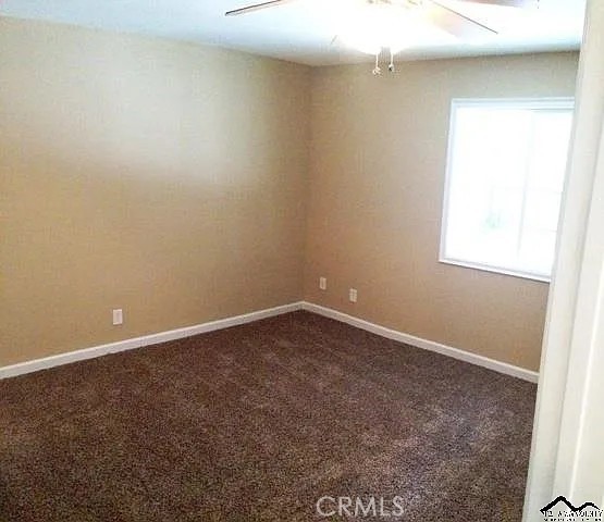 unfurnished room with dark colored carpet, baseboards, and a ceiling fan