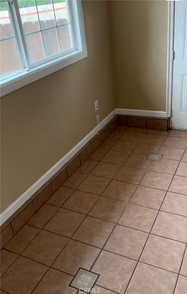empty room with baseboards, a healthy amount of sunlight, and light tile patterned flooring
