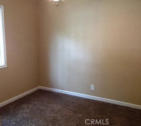 unfurnished room with baseboards and dark carpet