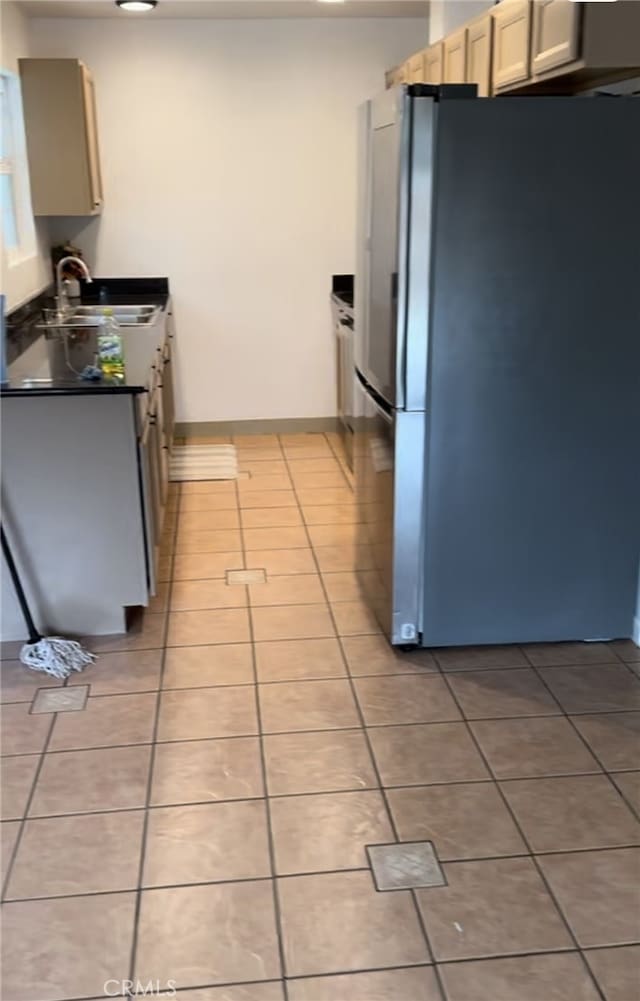 kitchen featuring freestanding refrigerator, dark countertops, light tile patterned flooring, and a sink